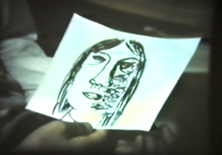 A hand holds a piece of paper with a face drawn on it. 