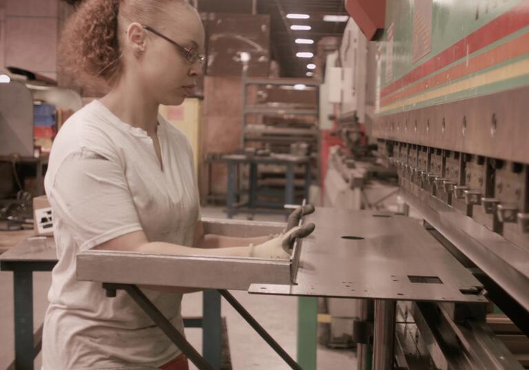 A worker holds a piece of metal against a machine. 