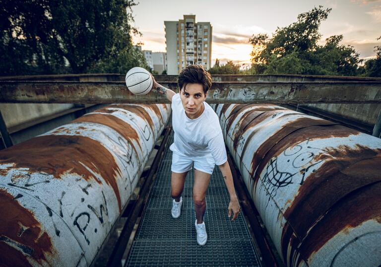 Basketball player and activist Katsiaryna Snytsina plays baketball between two pipes in an industrial setting.