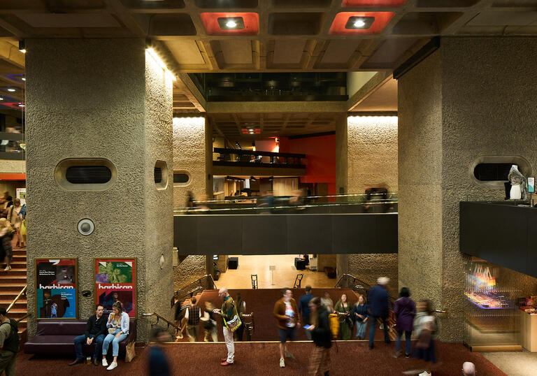 A candid photograph of lots of people sitting or standing in the Barbican Mezzanine foyer