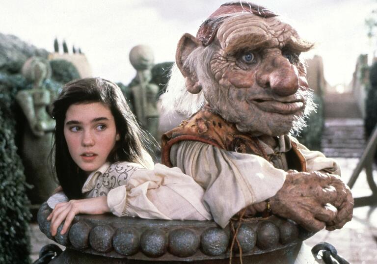 A young woman and goblin pop their heads above a pipe.