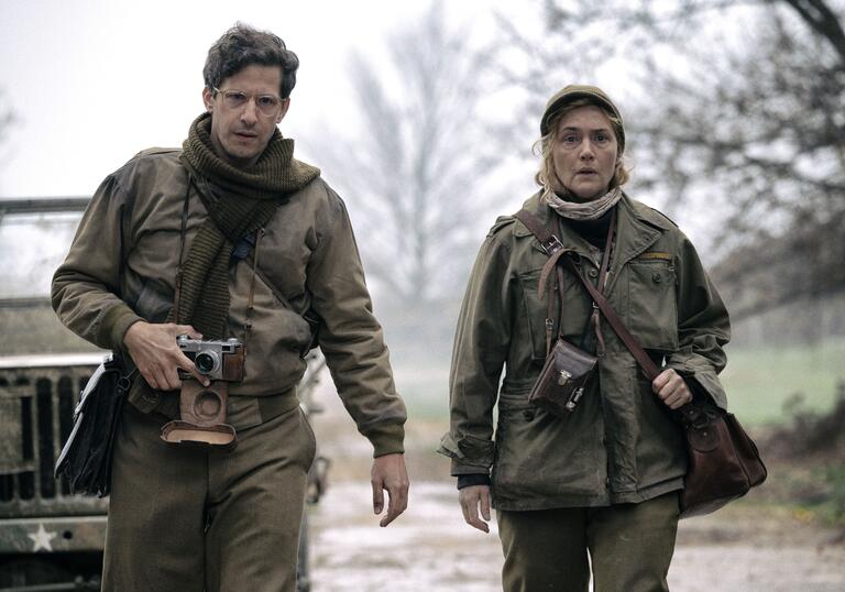 Two people in US Army fatigues walk down a road with cameras around their necks.