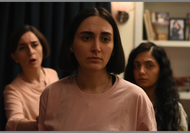 Three women look concerned inside an apartment. 