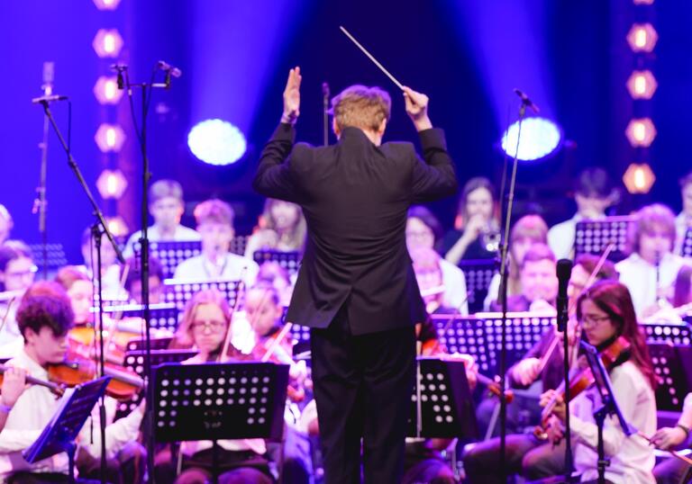 A school orchestra on stage with a conductor standing in front of them