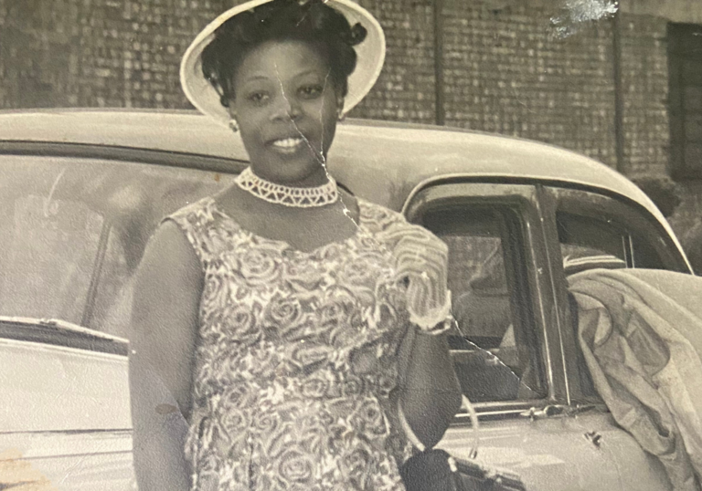 A black and white photograph of a black woman in a floral dress and white hat