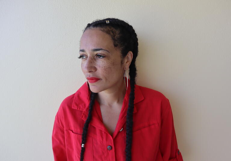 A photo of Zadie Smith wearing red lipstick and a red top, looking into the distance. 