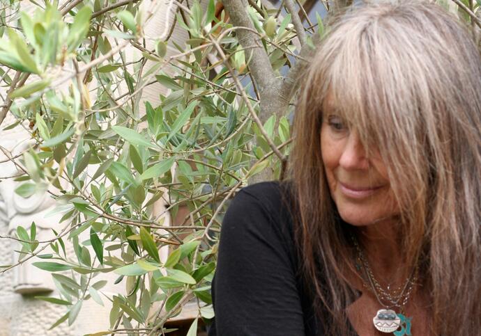 Vashti Bunyan in front of a tree, wearing a black top and long necklaces