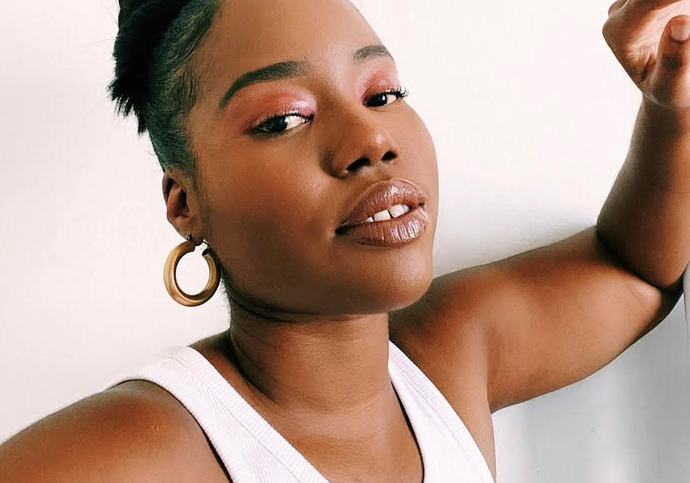 headshot of woman called DJ Sky, she is a black woman leaning on a white wall in a white vest.