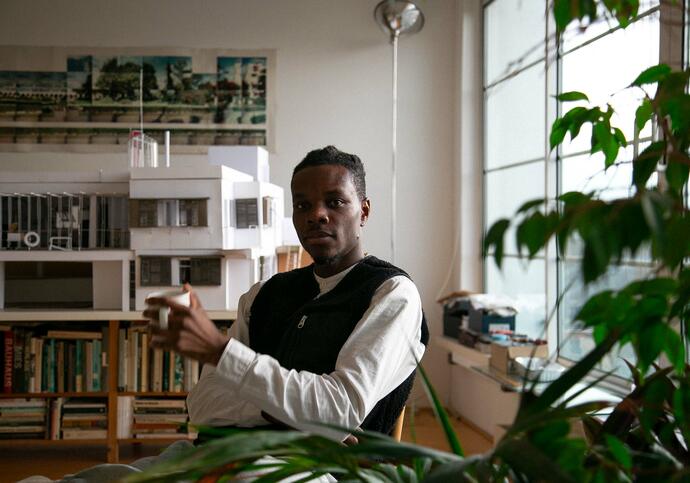 Image of man sat in chair wearing white shirt, black sweater vest holding a mug