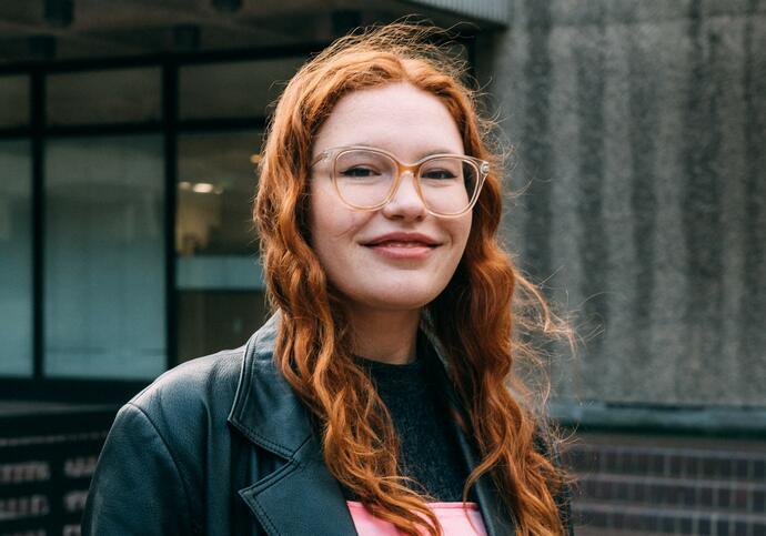 Person with long ginger hair and glasses smiling