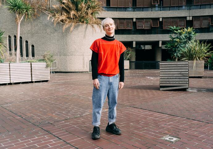 Person in red top and jeans standing in front of Barbican estates