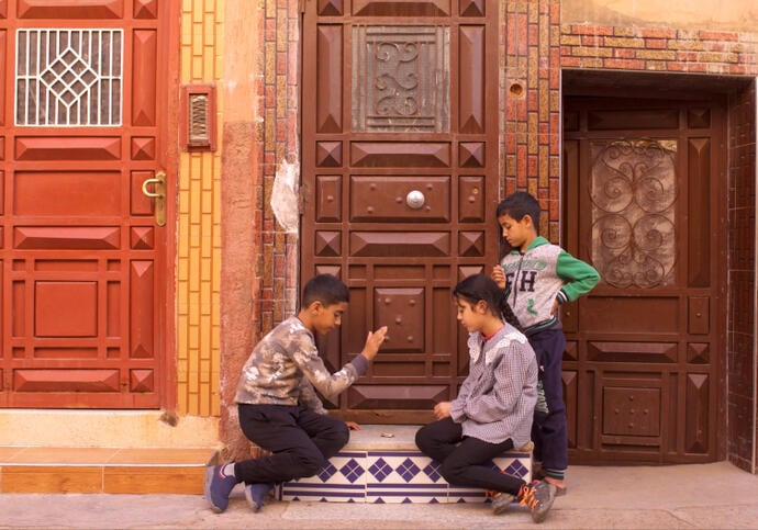 Image of three children sitting and standing by a brown door
