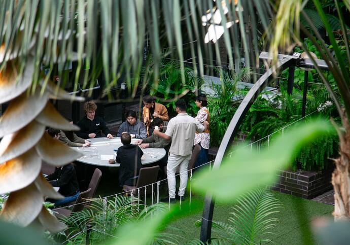 Group of secondary school children crafting around a table in the conservatory, surrounded by plants