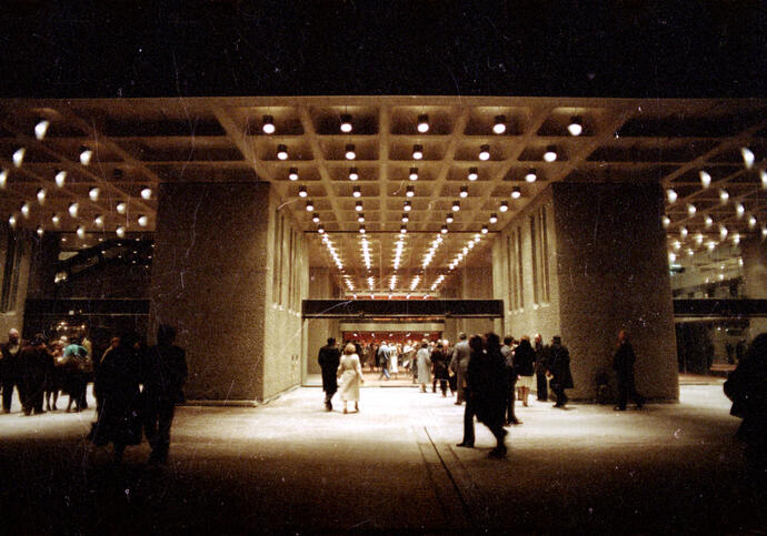 A night time photo of the Lakeside entrance of the Barbican, with bright overhead lights and people walking around