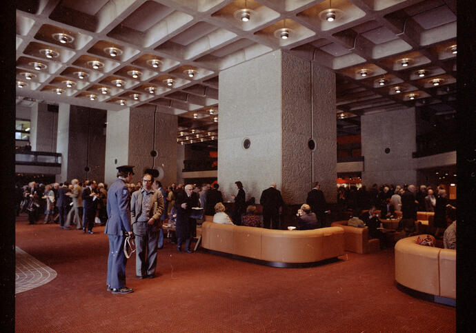 A busy foyer space with curved brown leather sofas and people sitting and standing at the Barbican in 1982