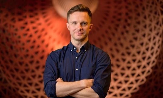 James McVinnie stands in front of a big orange dome, with his arms crossed