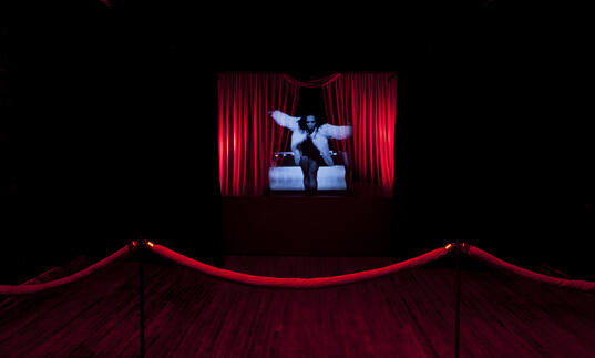 Woman in blue light on the middle of a stage with red curtains on either side