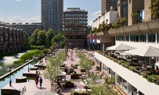 A photo along the Barbican Lakeside in bright sunshine, with a tower at the far end