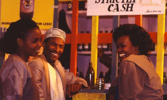 Two women and a man laugh whilst standing in front of a shop front.