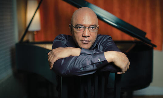 Billy Childs resting on folded arms, with grand piano in background