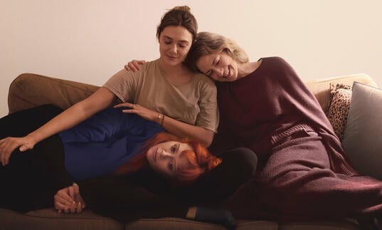 Three sisters sit on a sofa hugging each other. 