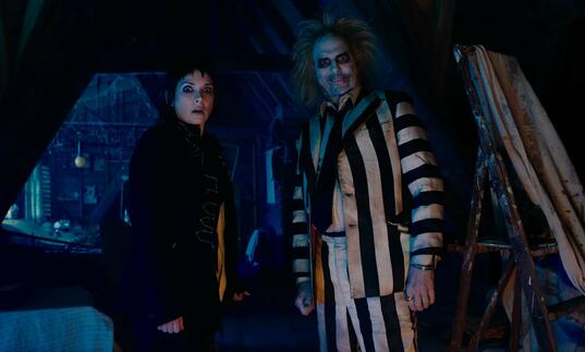 Lydia Deetz and Beetlejuice stand in a dark attic