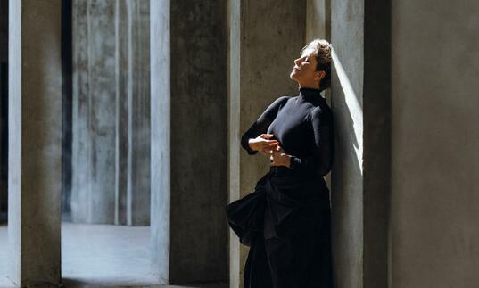 Joyce DiDonato in a black dress, leaning with her back against a wall