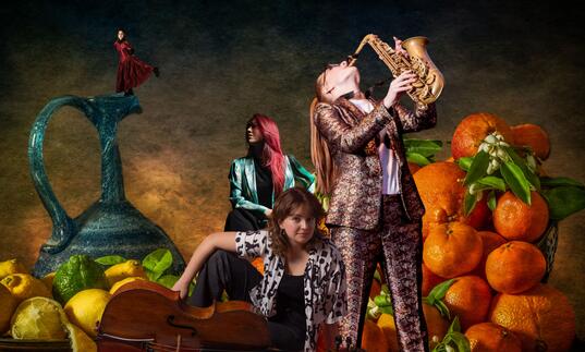 Jess Gillam playing the saxophone in front of a pile of giant oranges