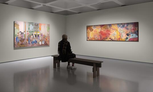 a person sits on a bench in front of two paintings