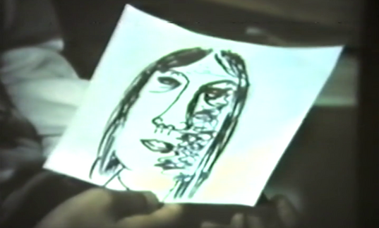 A hand holds a piece of paper with a face drawn on it. 