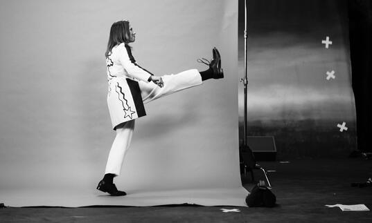 Profile of Kim Deal kicking leg up, in photo studio