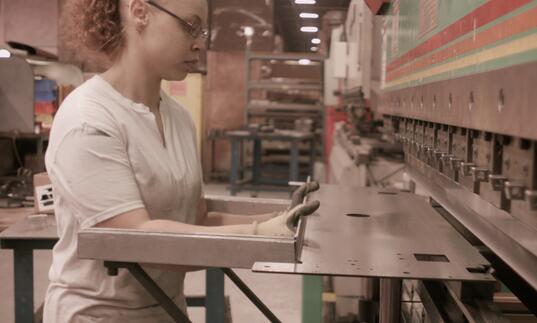 A worker holds a piece of metal against a machine. 