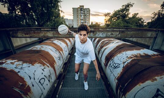 Basketball player and activist Katsiaryna Snytsina plays baketball between two pipes in an industrial setting.