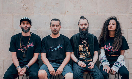 A portrait of band DAM, three men and a woman dressed casually in black t-shirts and denim and looking into the camera