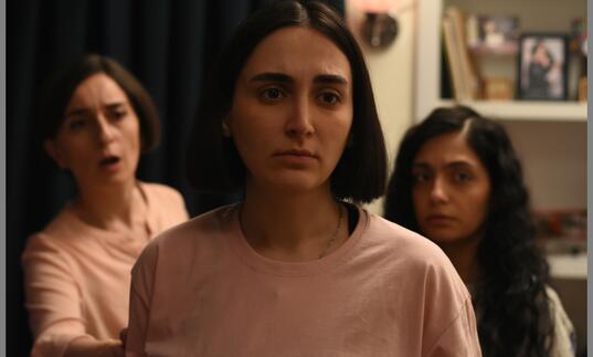 Three women look concerned inside an apartment. 