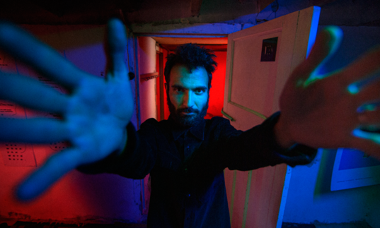 A man with hark hair and beard with his hands extended forward reaching for the camera