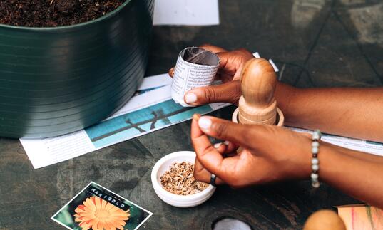 A close-up image of a pair of hands at a workshop, working with flowers and tea leaves.