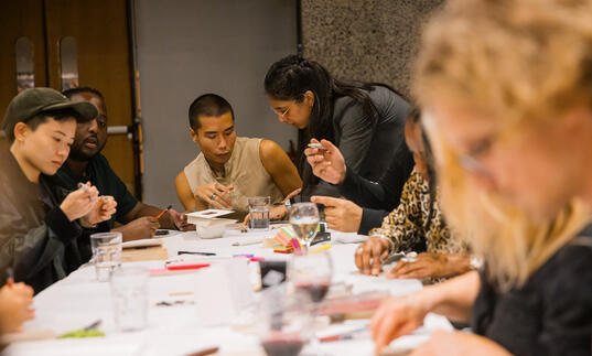 Image of multiple people sat around a long desk with a white cover making slime